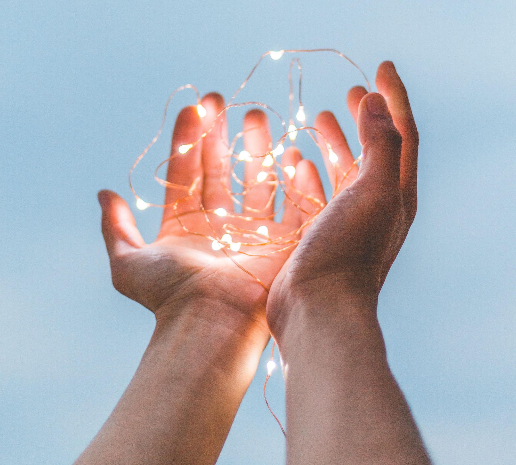 Image of two hands holding a string of white lights to symbolize embrace of an idea